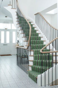 White hallway with black spiral staircase and green striped carpet
